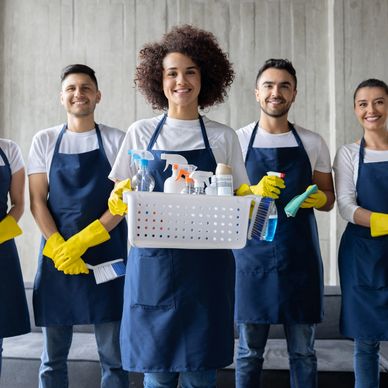 A diverse cleaning team wearing aprons and gloves, holding cleaning supplies.