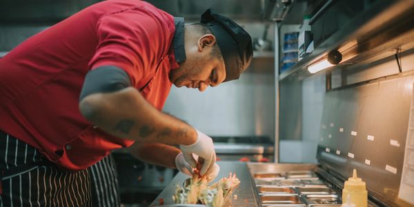 Chef in red shirt carefully preparing food in a professional kitchen.