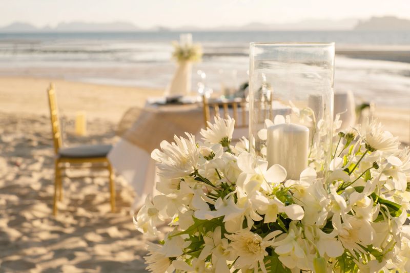 Beautiful table set up for a romantic dinner on the beach with  flowers and candles. Catering for a romantic date, wedding or honeymoon background. Sunset beach dinner. selected focus.