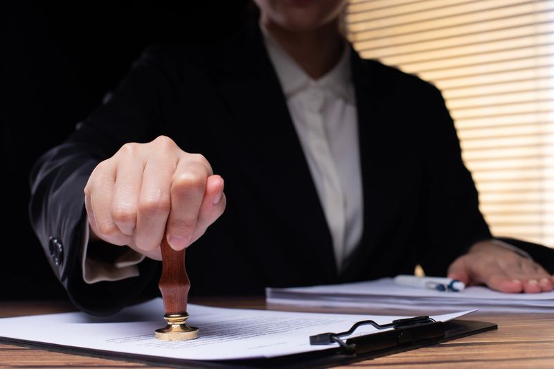 Person Signing Approval document, certificate, legal agreement in office by pen and stamp hand. Authority apply law to do contract paperwork form by public notary clerk or official lawyer, copy space