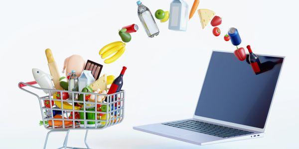 Groceries flying from a shopping cart into a laptop, symbolizing online grocery shopping.