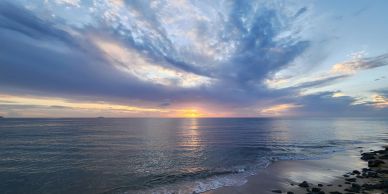 Sunset over a calm ocean with scattered clouds.