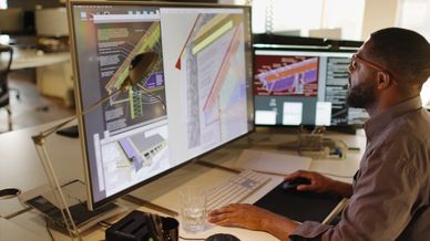 Man working on architectural designs on a computer with dual monitors.
