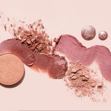 Various crushed and spread pink and bronze makeup powders on a light background.
