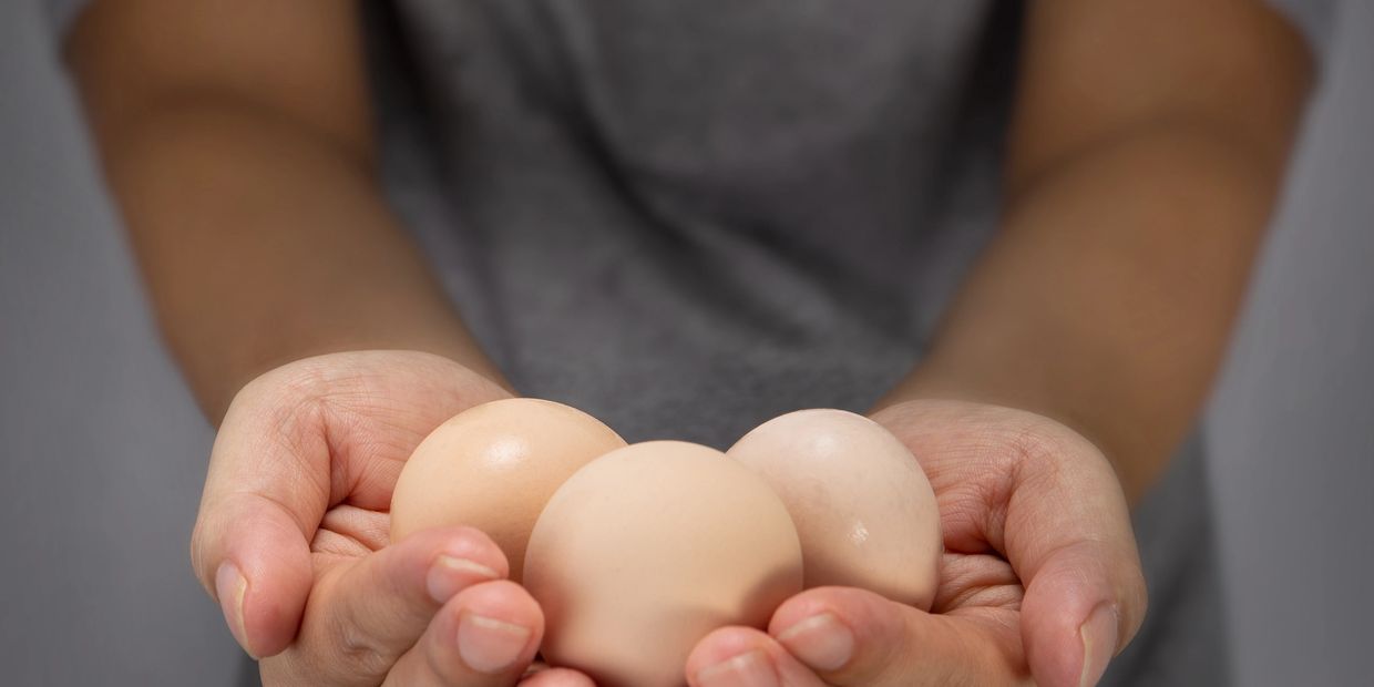 Hands holding three brown eggs gently.
