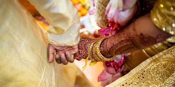 Close-up of a couple's hands during an Indian wedding ceremony with henna and gold attire