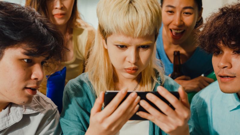 Close-up Group of happy Asian teenage people sit on couch watch cheer sport soccer games world cup championship together on smartphone. Shouting strike goal excited scream, facial expression concept.