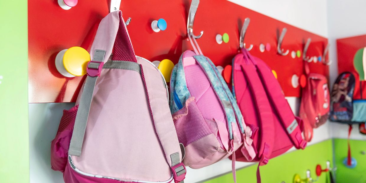 Colorful backpacks hanging on hooks in a classroom.