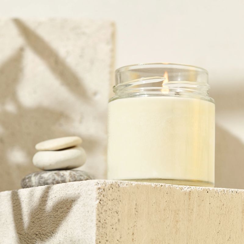 Aesthetic composition with aromatic candle in jar on concrete podium. Mockup soy wax candle in natural style. Scented handmade candle with green leaves.  Handmade spa product  from soy wax in glass