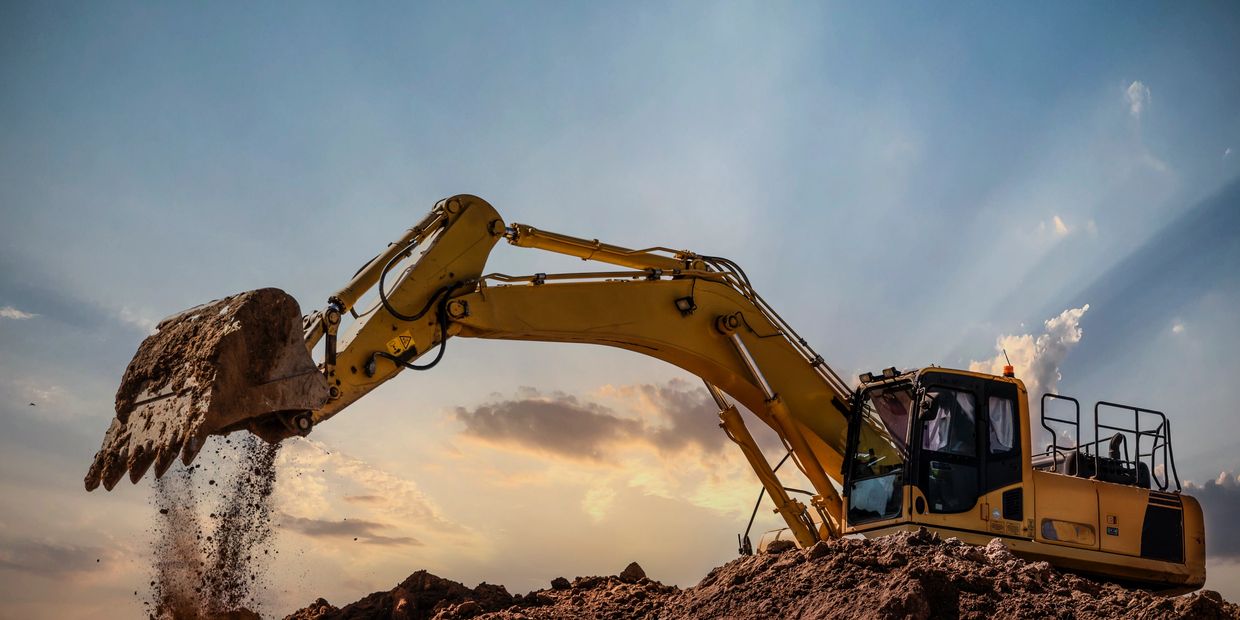 Yellow excavator scooping dirt at a construction site during sunset.