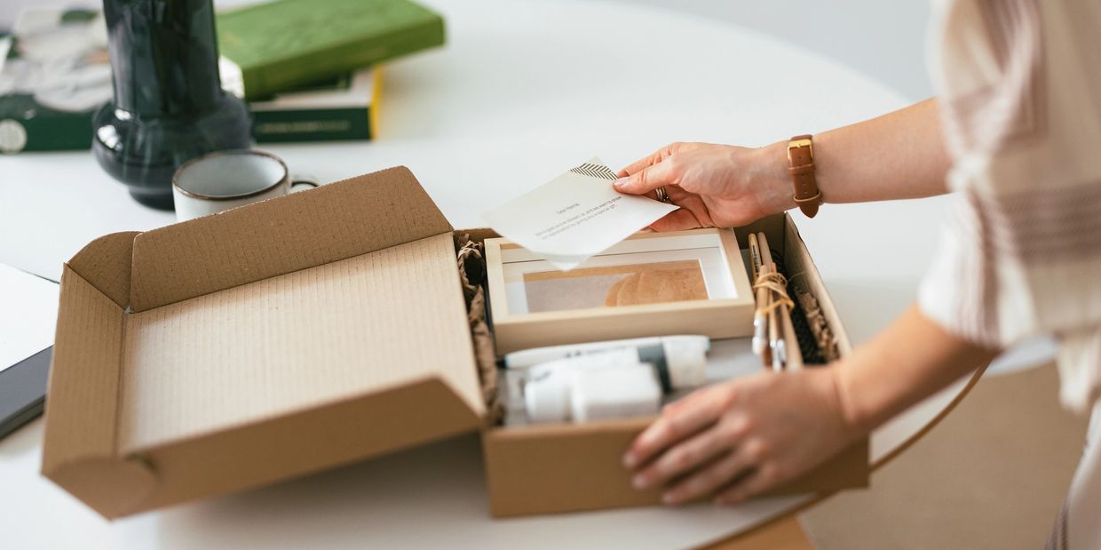 Person opening a brown cardboard gift box with art supplies inside.