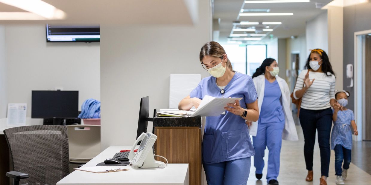 Healthcare workers in masks working and walking through a medical facility hallway.