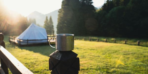 Metal cup on a wooden post with a tent and sunrise in the background.