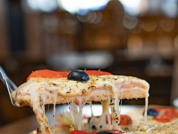 A slice of cheesy pizza with black olives being lifted.