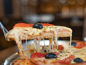 A slice of cheesy pizza with black olives being lifted.