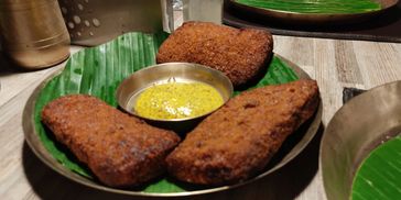 Three pieces of fried Indian snacks served on a banana leaf with chutney.