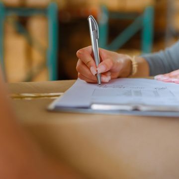 Person signing a document on a clipboard with a silver pen.