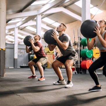 Three people exercising with medicine balls in a gym.