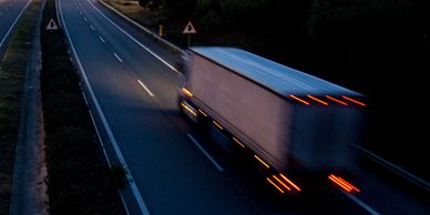 A large truck speeding on a highway at dusk with blurred motion.