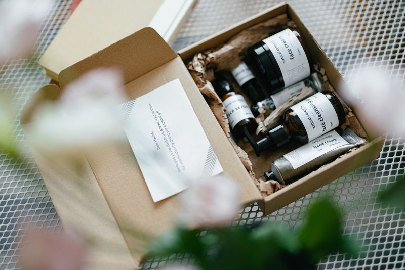 Shot from above of an open gift box on the coffee table. There are natural cosmetic products inside and paper note.