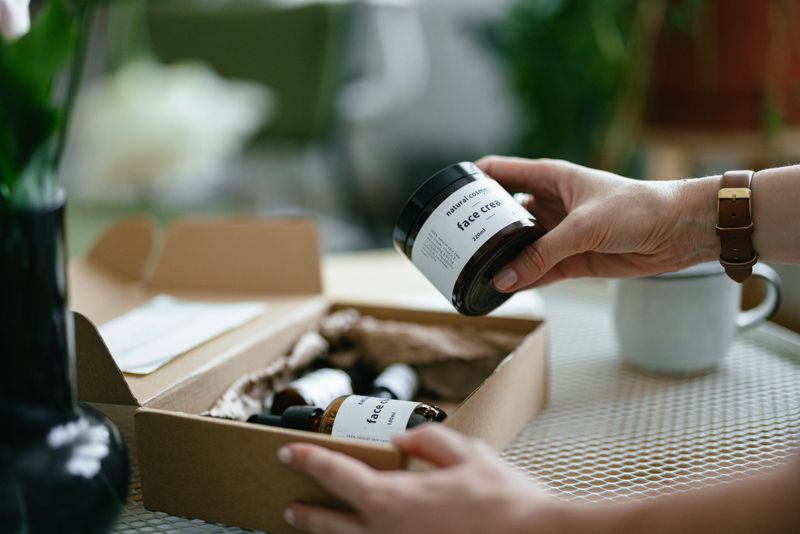 Close up shot of an anonymous woman trying out products from a carton gift box. There are various natural beauty cosmetics products inside and a personal paper note.