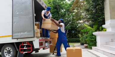 Two movers unloading cardboard boxes from a truck at a house.