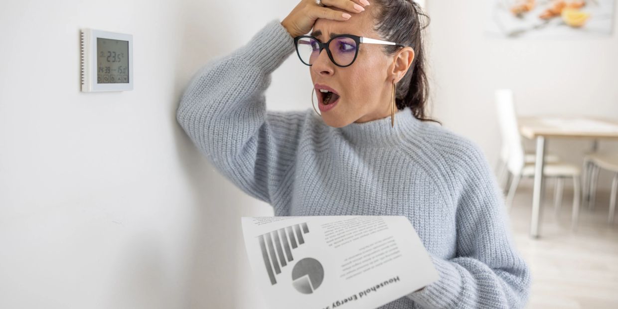 Woman shocked by energy bill while checking thermostat.