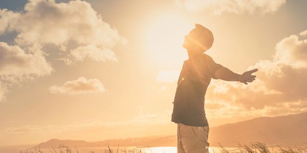 Person enjoying the warm glow of a sunset with open arms in a grassy field.