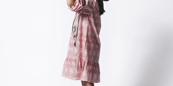 Woman in a pink patterned dress posing against a white background.
