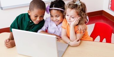 Three children happily looking at a laptop.