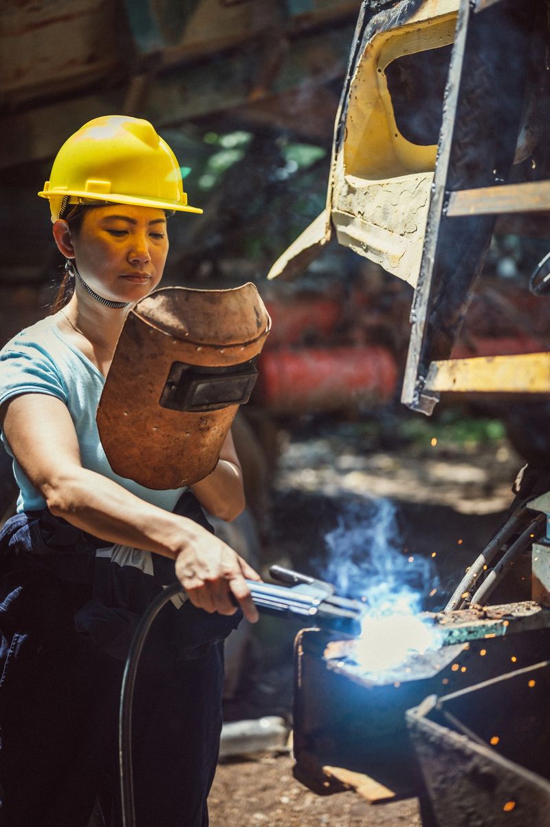 An Asian Chinese Female Industrial Welder holding welding Torch with welding sparks at construction site