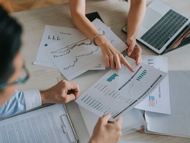 Two people discussing financial charts and data at a desk with a laptop.