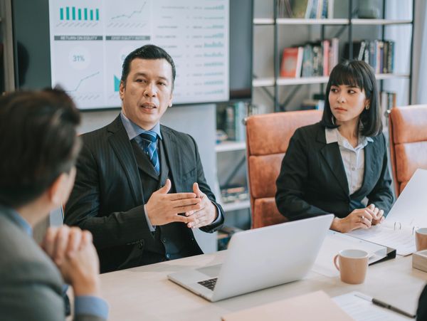 Two people having a meeting, one holding a laptop and the other holding glasses.