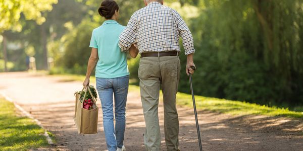 Elderly couple walking arm in arm on a sunny park path.