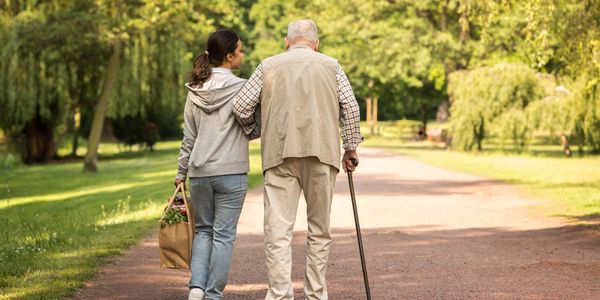 Young woman walks arm-in-arm with elderly man in park.