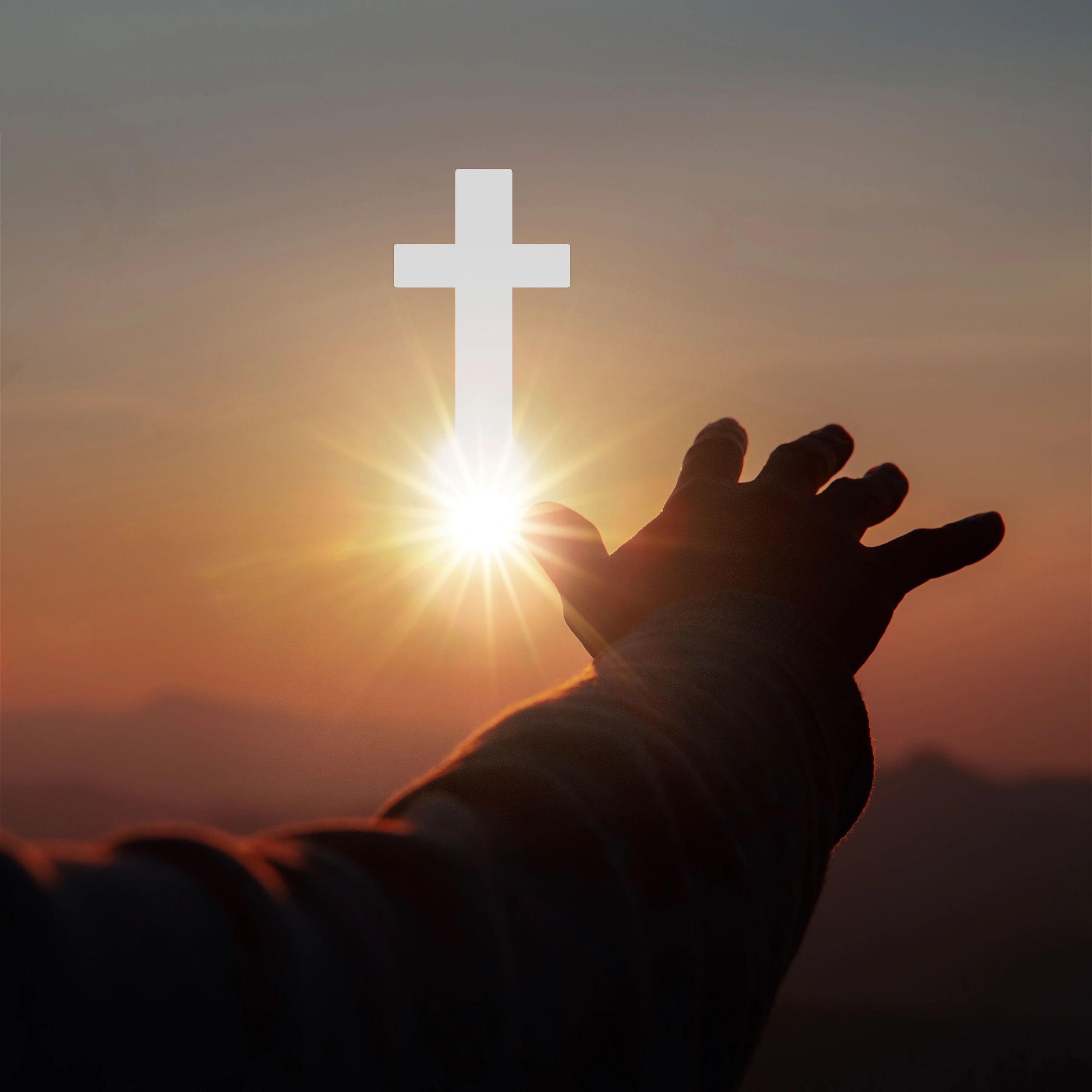 Hand reaching towards a glowing cross at sunset symbolizing faith.