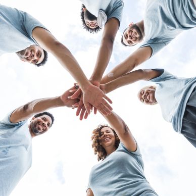 Group of people joining hands in a circle, smiling.
