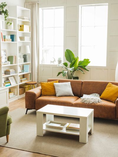 Bright living room with brown sofa, white coffee table, and tall windows.