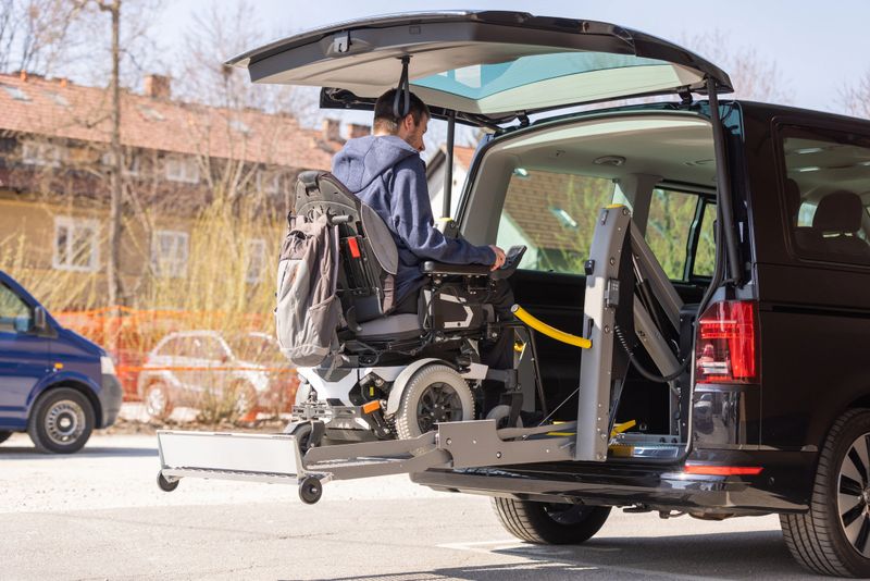 Man with disability using hydraulic wheelchair lift to get in the van, after a summer day spent on beautiful mountain nature