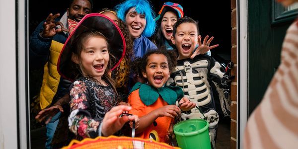 Children and adults in Halloween costumes excitedly trick-or-treating at a door.