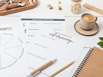 Workspace with self-discovery journal prompts, SMART goal worksheet, and coffee.
