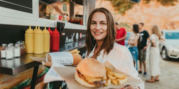Smiling woman holding a burger and fries at an outdoor food stand.