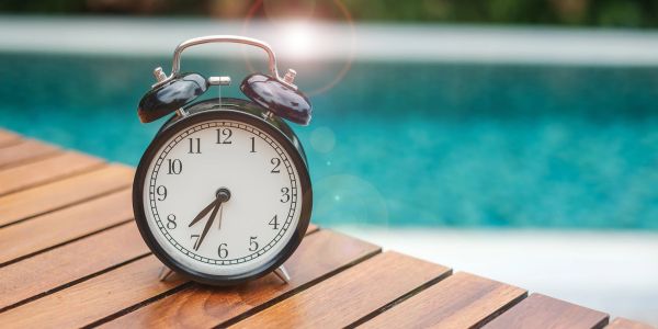 A clock on a wooden surface by a pool.