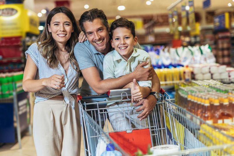 Happy family with child and shopping cart buying food at grocery store or supermarket