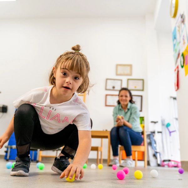 Young girl crouching and picking a ball indoors.
