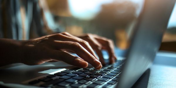 Close-up of hands typing on a laptop keyboard in soft lighting.