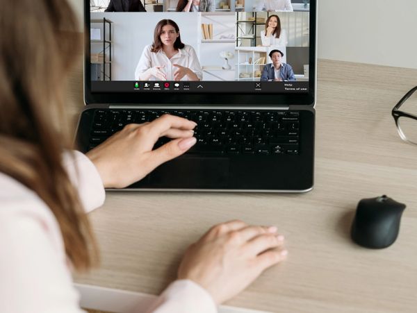 A person participates in a video conference with six colleagues on a laptop.