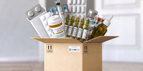 Cardboard box filled with various medicines, syringes, and vaccine vials.