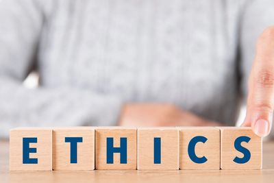 Wooden blocks spelling 'ETHICS' with a person pointing at the last block.