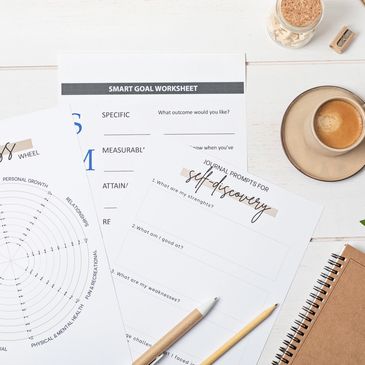 Wellness and self-discovery worksheets with coffee and stationery on a white desk.